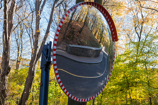 Convex spherical traffic panoramic mirror, mounted on a bend of local road with reflection of the winding forest road section in him in sunny autumn day