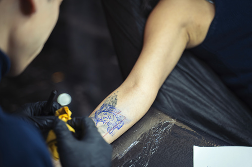 Tattoo master making tattoo on customer's arm