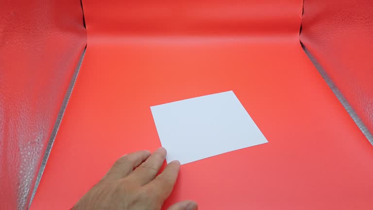 Man's hand holding and writing on white paper with red background.