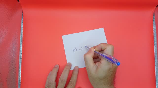 Man's hand holding and writing on white paper with red background.