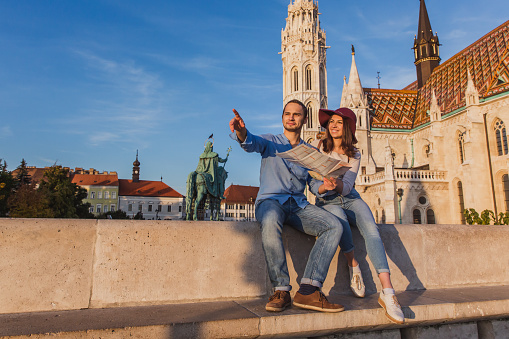 Young couple searching right direction on map from the point from Fisherman Bastion in Budapest with Matthias Church on background during sunrise