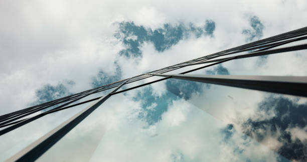 Low angle, skyscraper building and clouds in city with reflection, nature and urban infrastructure. Architecture, cityscape and skyline and metro with landscape, glass and sky background in timelapse