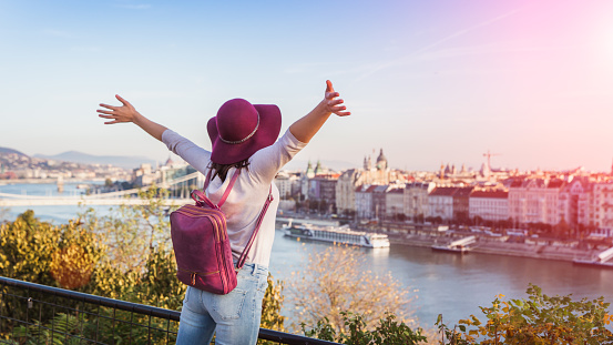 A happy young woman in purple hat enjoying her trip to Budapest, Hungary from the point from Gellert Hill during sunrise in autumn during sunrise.