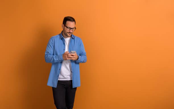 istock Smiling handsome businessman using social media apps over mobile phone on isolated orange background 2055517619