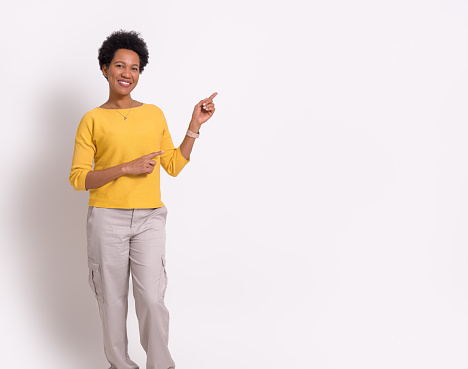 Portrait of smiling young businesswoman with afro hair pointing at copy space on white background