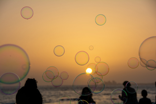 Many colorful soap bubbles float in the orange sky at sunset wiwth people in silhouette
