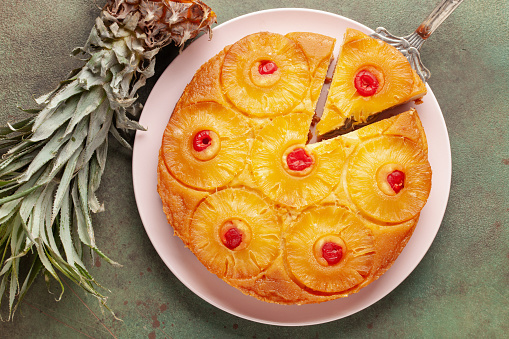 Homemade pineapple upside down pie with candied cherries . Tropical dessert on green background. Top view