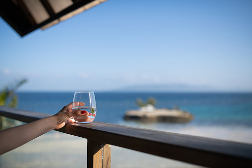 Woman's hand holding a glass of water at a restaurant by the sea