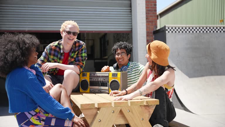 Smiling friends sitting at picnic table with boom box