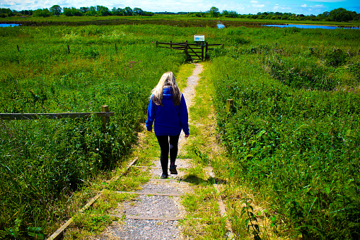 A lone woman walks through the countryside on a beautiful sunny afternoon