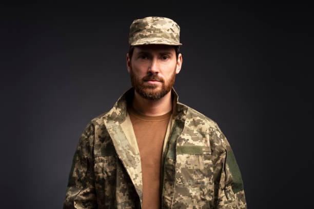 istock Serious soldier wearing camouflage military uniform looking at camera isolated on black background 2055820479
