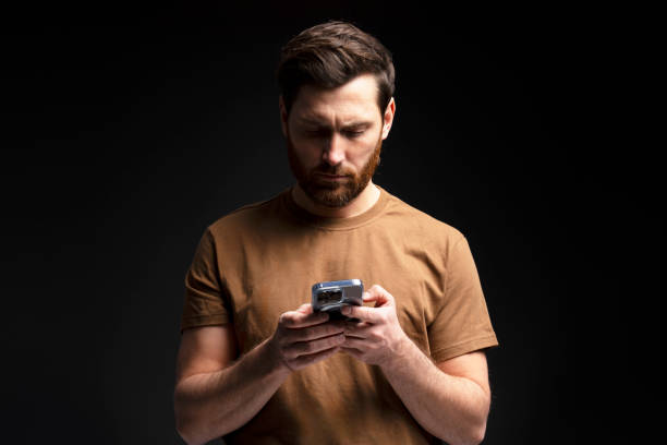 istock Serious man holding mobile phone text message, communication online isolated on black background 2055821013