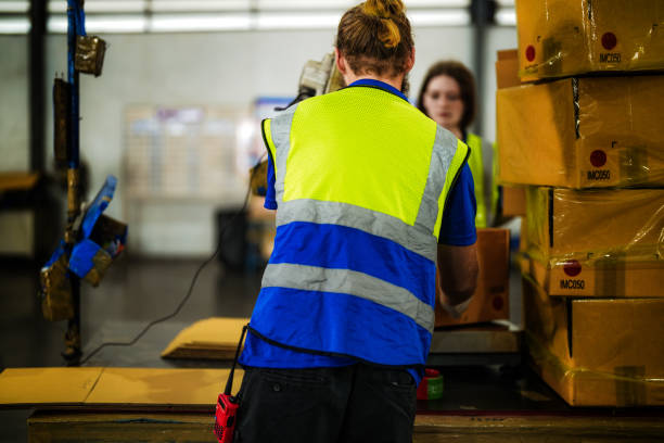 istock Warehouse worker folding paper box for packing the items in a large warehouse. man sealing cardboard boxes for shipping in cargo product stock. 2055865446