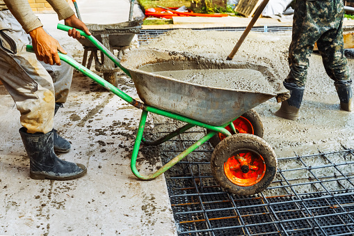 Pouring concrete after placing steel reinforcement, concrete mixing. A worker uses a wheelbarrow to transport liquid concrete to pour a concrete slab.