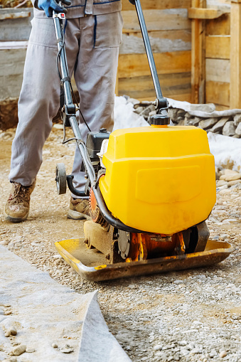 Builder Worker at sand ground compaction with Vibration plate compactor machine before pavement Roadwork, Vibratory plate