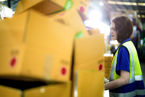 Warehouse woman worker folding paper box for packing the items in a large warehouse. man sealing cardboard boxes for shipping in cargo product stock.