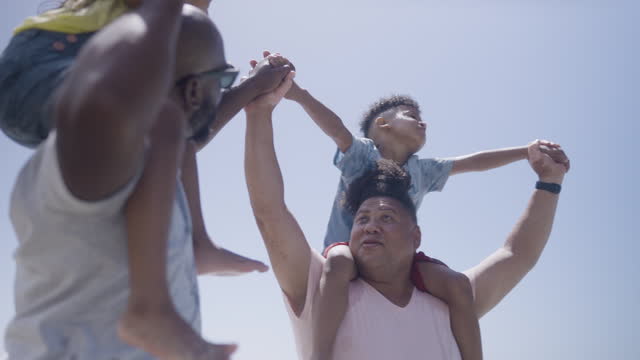 Gay couple with two children on shoulders playing on beach