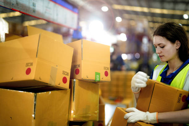 istock Warehouse woman worker folding paper box for packing the items in a large warehouse. man sealing cardboard boxes for shipping in cargo product stock. 2055901889