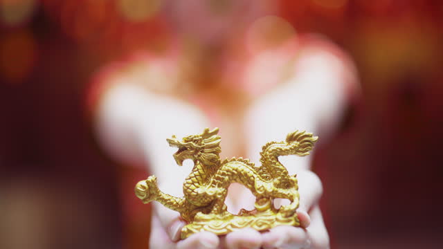 young asian girl in red Cheongsam gives you the gold dragon ingot she is holding.smiling broadly and glancing at the camera.chinese new year concept.