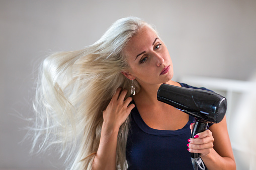 Young blonde woman dry her hair