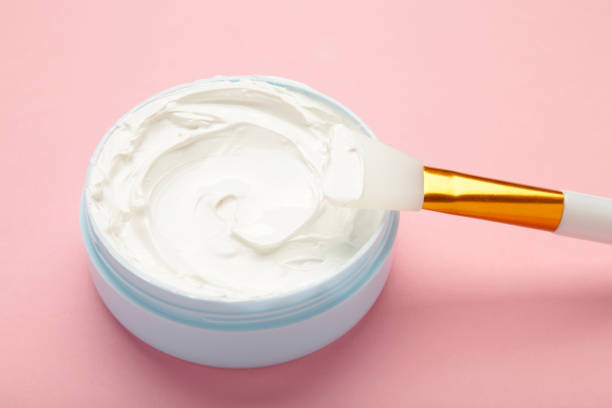 istock Cosmetic mask (scrub) in a bowl with brush on pink background. 2055944421