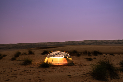 One men in illuminated small tent in Wahiba desert in Oman at night.