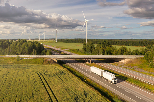 A semi-truck with trailer on a highway through a rural landscape with wind power stations. Örebro county, Sweden.