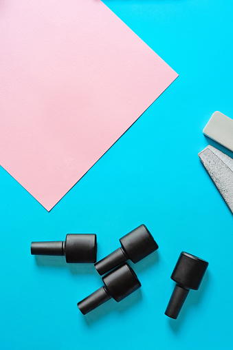 Several gel polishes in black jars and several nail files of different hardness, you can see on them that they have been used. on soft pink-blue. Beauty saloon. Lifestyle. Manicure. Time for yourself.