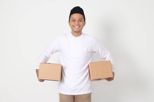 Portrait of attractive Asian muslim man in koko shirt with peci feeling grateful and peacful while carrying cardboard box. Going home for Eid Mubarak. Isolated image on white background Portrait of attractive Asian muslim man in koko shirt with peci feeling grateful and peacful while carrying cardboard box. Going home for Eid Mubarak. Isolated image on white background peacful stock pictures, royalty-free photos & images