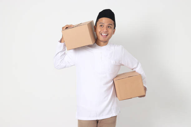 Portrait of attractive Asian muslim man in koko shirt with peci feeling grateful and peacful while carrying cardboard box. Going home for Eid Mubarak. Isolated image on white background Portrait of attractive Asian muslim man in koko shirt with peci feeling grateful and peacful while carrying cardboard box. Going home for Eid Mubarak. Isolated image on white background peacful stock pictures, royalty-free photos & images