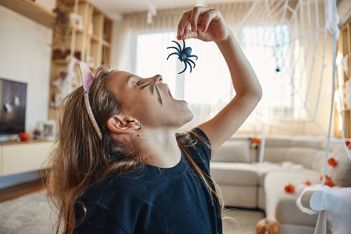 Beautiful girl on Halloween day dressed as a cat eating spider.