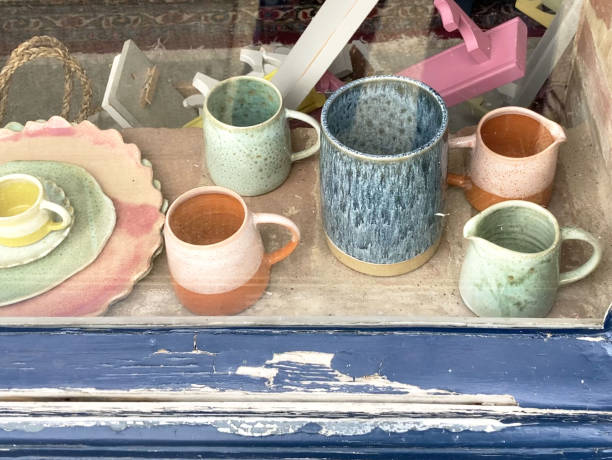 Pastel-coloured ceramics in an attractive display inside a shop window, with blue flaking paint on the window sill. Other items are arranged in a less organised way in the background