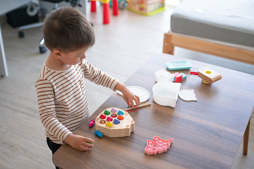 A two-and-a-half-year-old boy engages in imaginative play with a wooden toy fishing set, exploring the wonders of the underwater world from the comfort of his play area. This toy encourages motor skills development and hand eye coordination