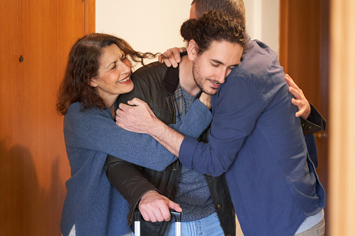 Emotional farewell concept. Son with suitcase hugging parents before moving out