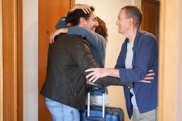 istock Son returns home concept. Parents hug young male with suitcase 2056122116