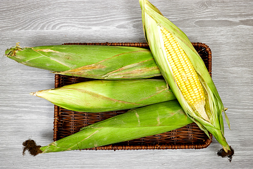 Fresh corn cob in esparto halfah basket isolated on wood table