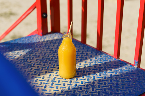 Natural mockup of orange or citrus juice in a glass bottle with a paper tube on a children's colored slide. thirst quenching during entertainment and children's drinks concept