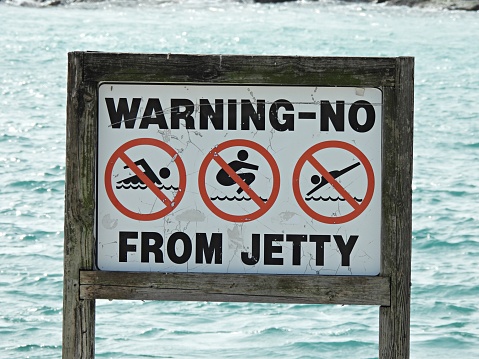Sydney, Australia - January 1, 2020: Young male tourist surfing in to the ocean with a red flag sign indicating no swimming or surfing at the ocean on Tamarama Beach, very near to famous Bondi Beach.