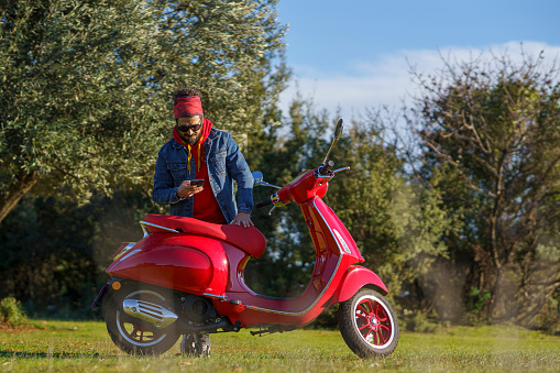Casual mid adult man posing with his scooter on grass taking a selfie