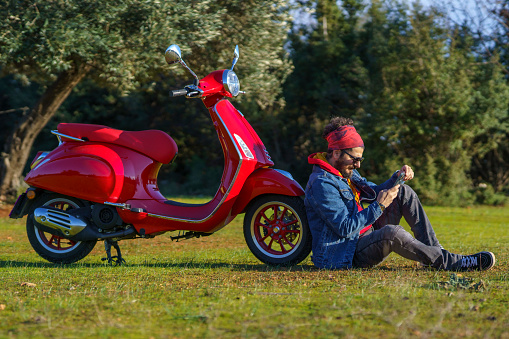 Casual mid adult man posing with his scooter on grass taking a selfie