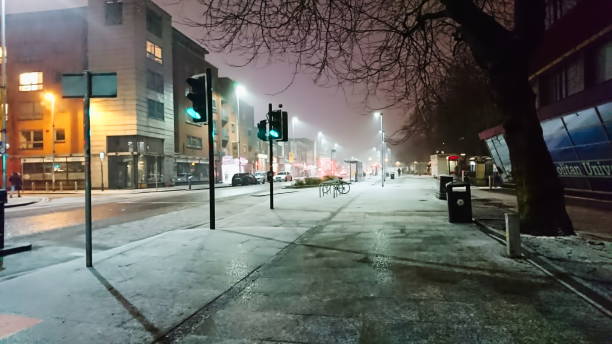 Manchester, UK - 02.11.2018: An empty pavement with a road on a snowy night next to Manchester Metropolitan University campus