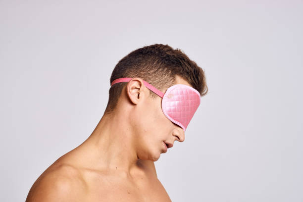 istock A man in a pink mask for sleeping on a light background at night gestures with his hands 2056277886