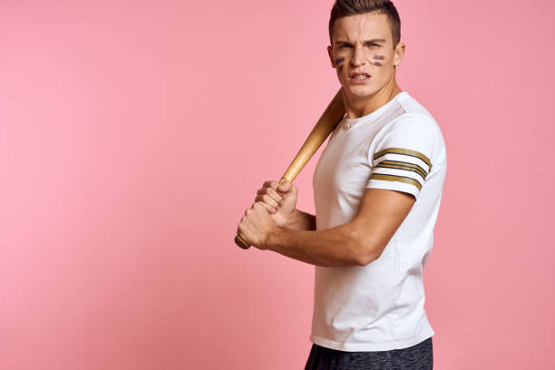 istock Energetic man with a bat on a pink background T-shirt face make-up black lines aggression model 2056305781