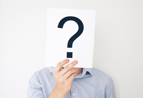 A man in a blue shirt holding a question mark in front of his head, white background, psychology concept