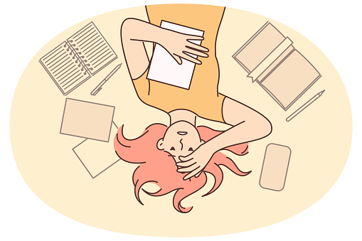 Woman student worry about upcoming exams at university or college lying on floor among textbooks. Girl student or office worker clutching head after experiencing burnout associated with overload