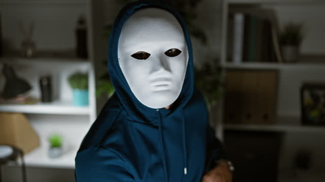 A mysterious person in a white mask and blue hoodie indoors creating a suspenseful atmosphere