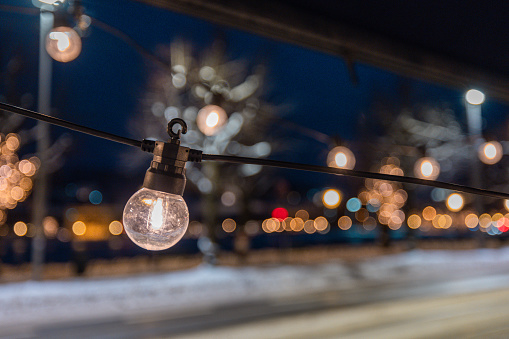 Light bulb as a christmas or decorative ornament. Closeup of a glass light. Other lights seen in blur in the background. Night setting outside.