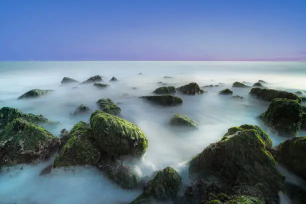 Rocks with green seaweed in the light of the setting sun and mystical waves . Long expusure photography on the dutch coast, Zeeland, Netherlands