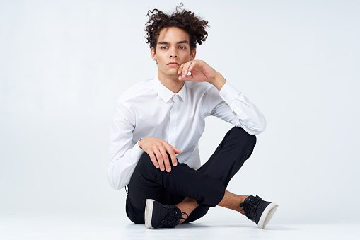a guy in trousers in sneakers and a shirt sits on the floor and gestures with his hands in full growth. High quality photo