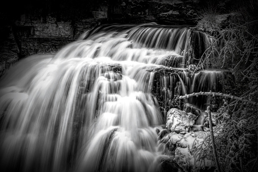 A close up black and white view of Inglis Falls near Owen Sound, Ontario as it crashes its way down the rocks and through the surrounding forest.